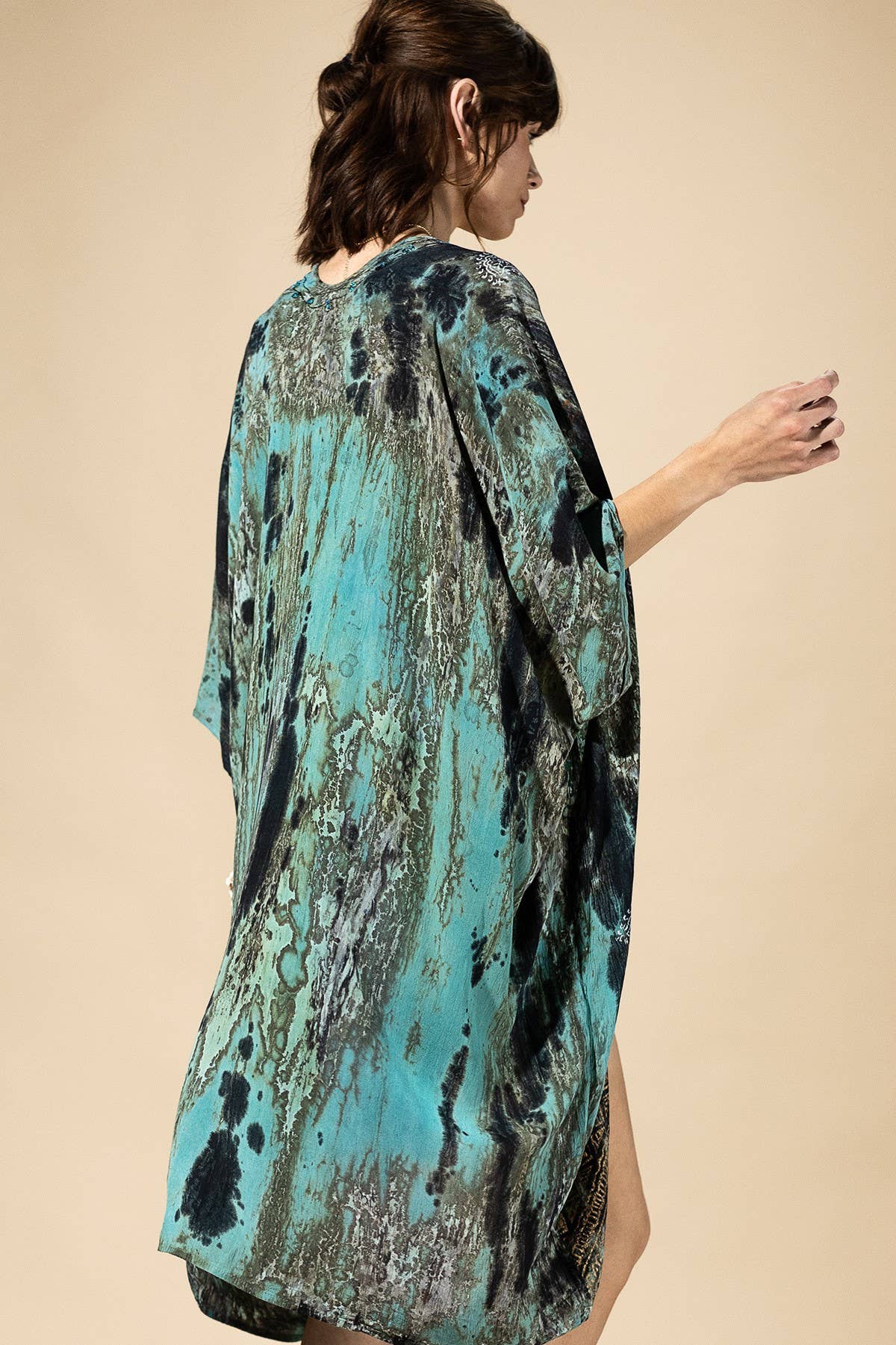 Woman wearing a turquoise and black patterned kimono-style garment on a beige background