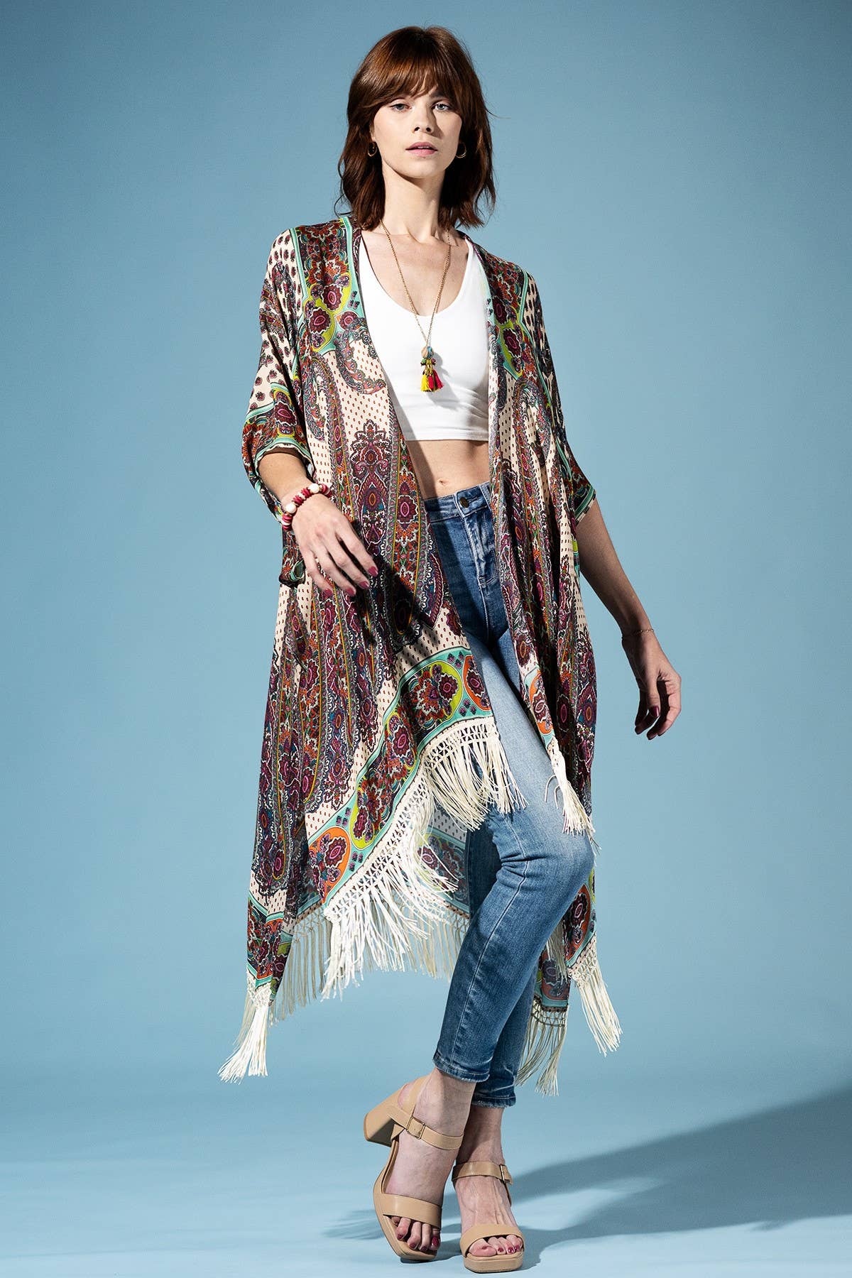 Woman wearing a patterned kimono over a white top and blue jeans on a light blue background