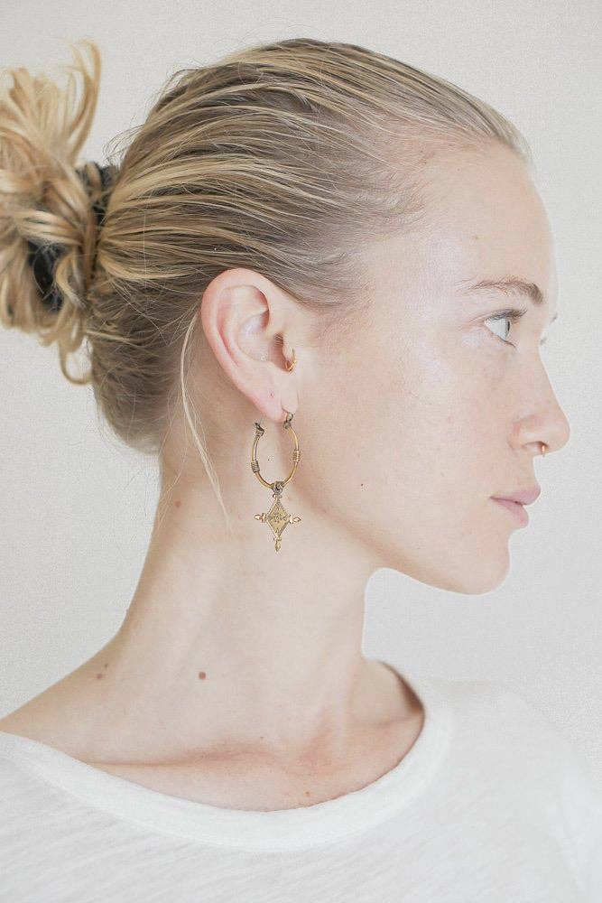 Side profile of a person with a bun and hoop earrings on a plain background