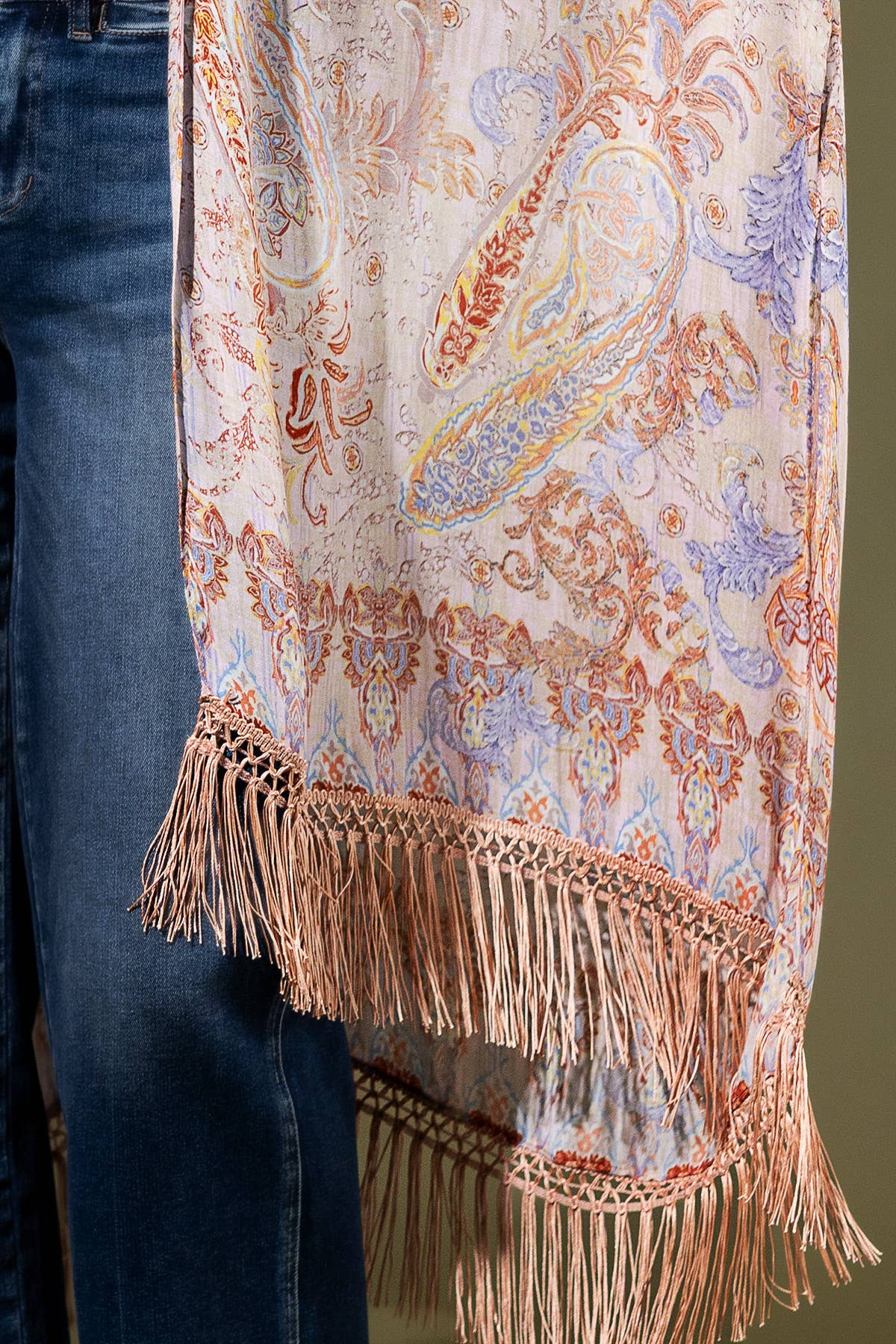 Decorative scarf with intricate patterns and fringes held by a person wearing jeans.