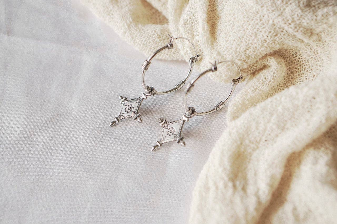 Silver hoop earrings with star-shaped charms on a textured beige fabric background