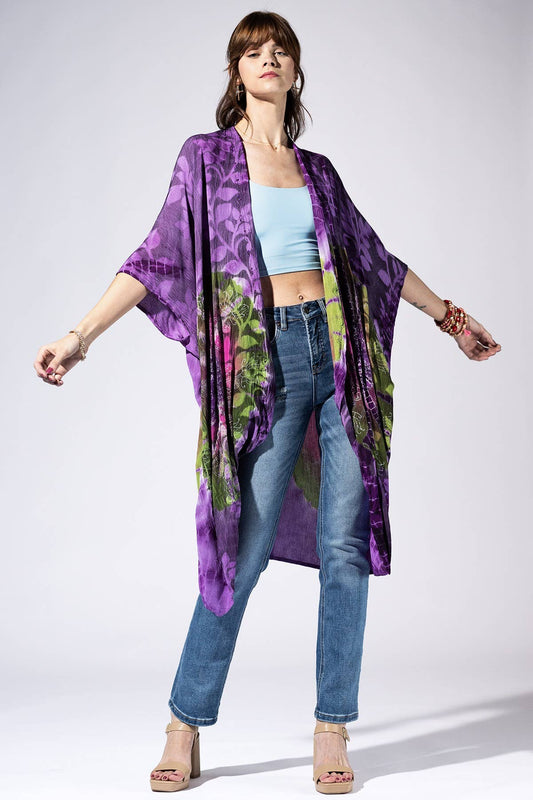 Woman wearing a purple floral kimono over a light blue top and jeans on a white background