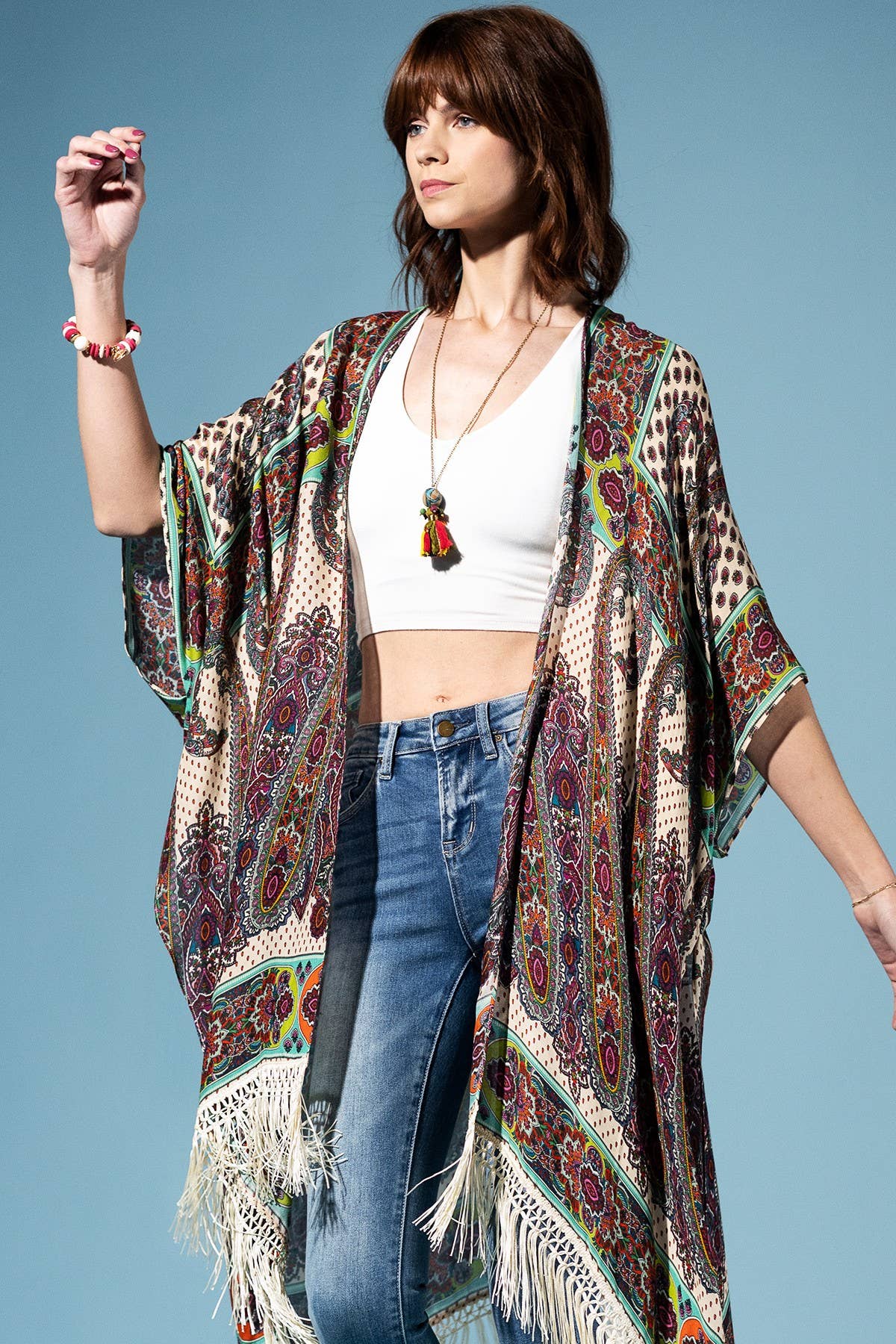 Woman wearing a patterned kimono over a white top and blue jeans on a light blue background