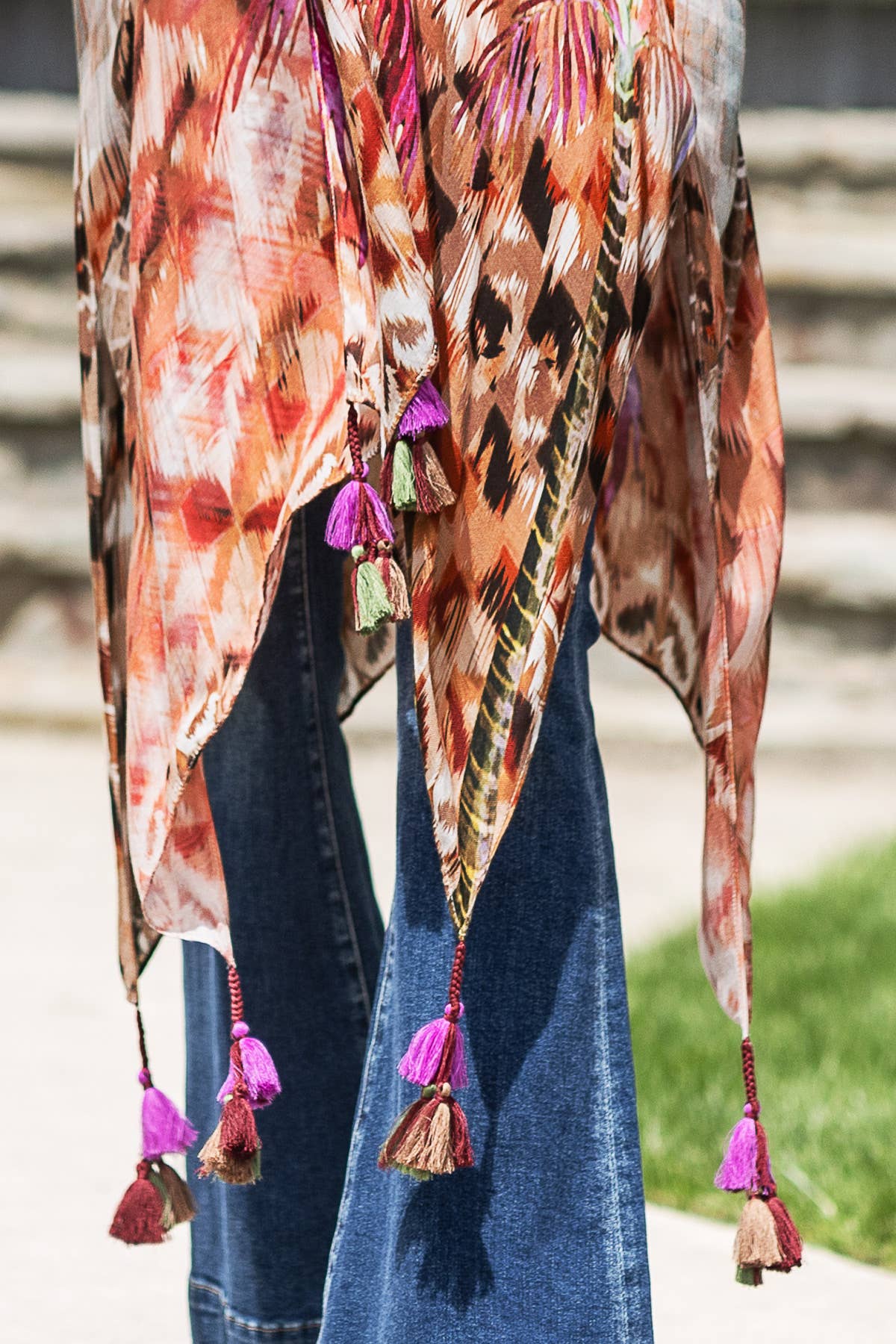 Colorful patterned shawl with tassels draped over a person wearing jeans, outdoors.