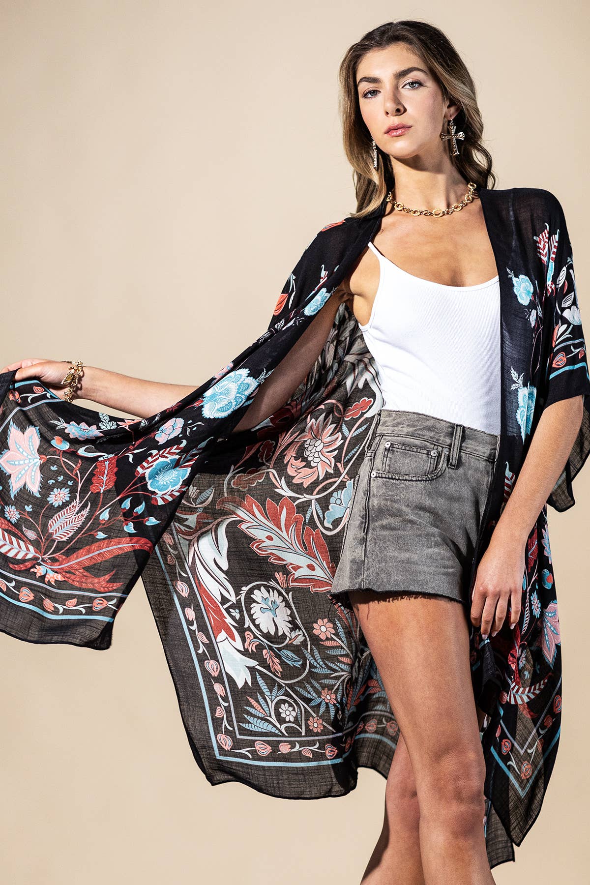 Woman wearing a floral kimono over a white top and gray shorts on a beige background