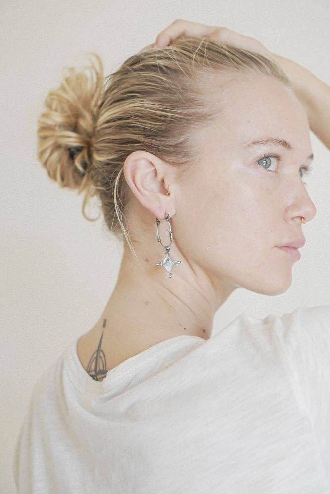 Woman with a bun hairstyle wearing earrings against a plain background