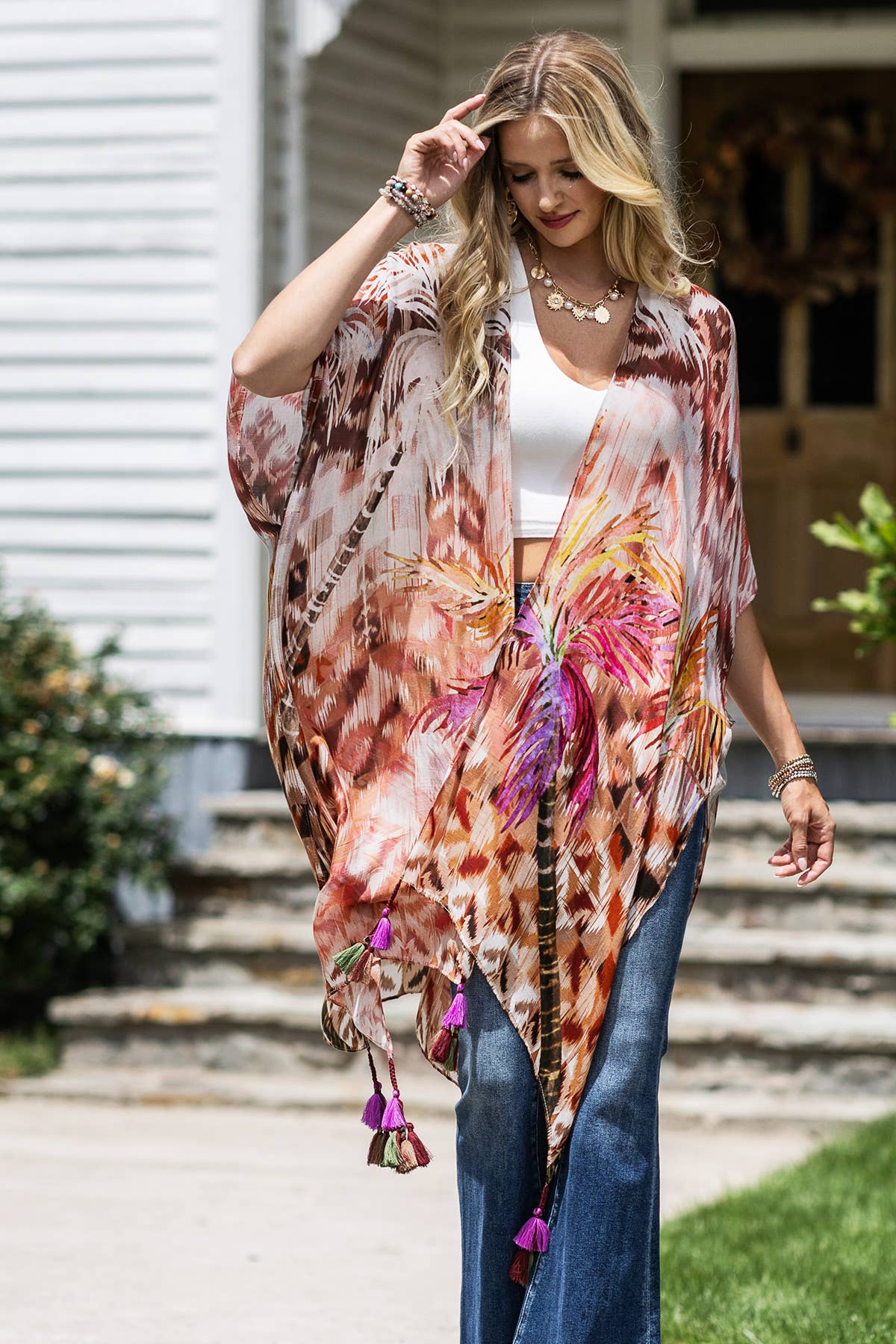 Woman wearing a colorful floral kimono with tassels in front of a house.