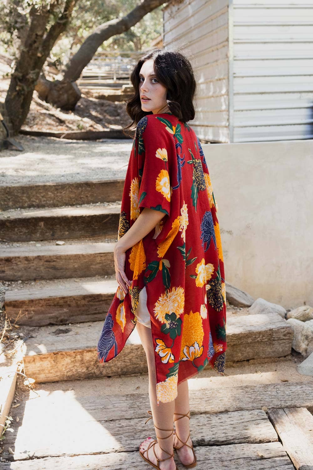 Woman wearing a colorful floral dress standing on wooden steps outdoors.