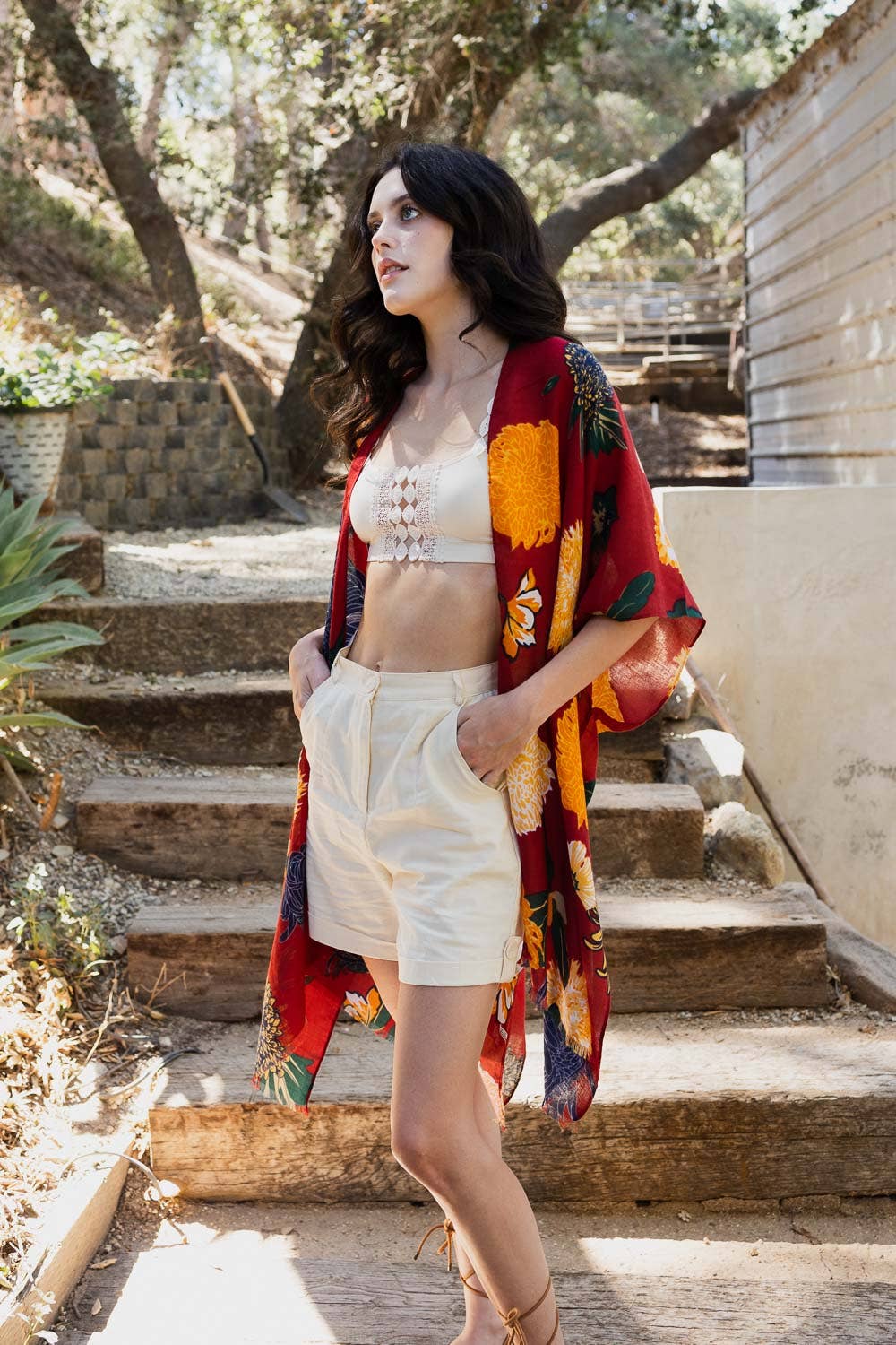 Woman standing on stone steps outdoors wearing a colorful shawl, white top, and shorts.