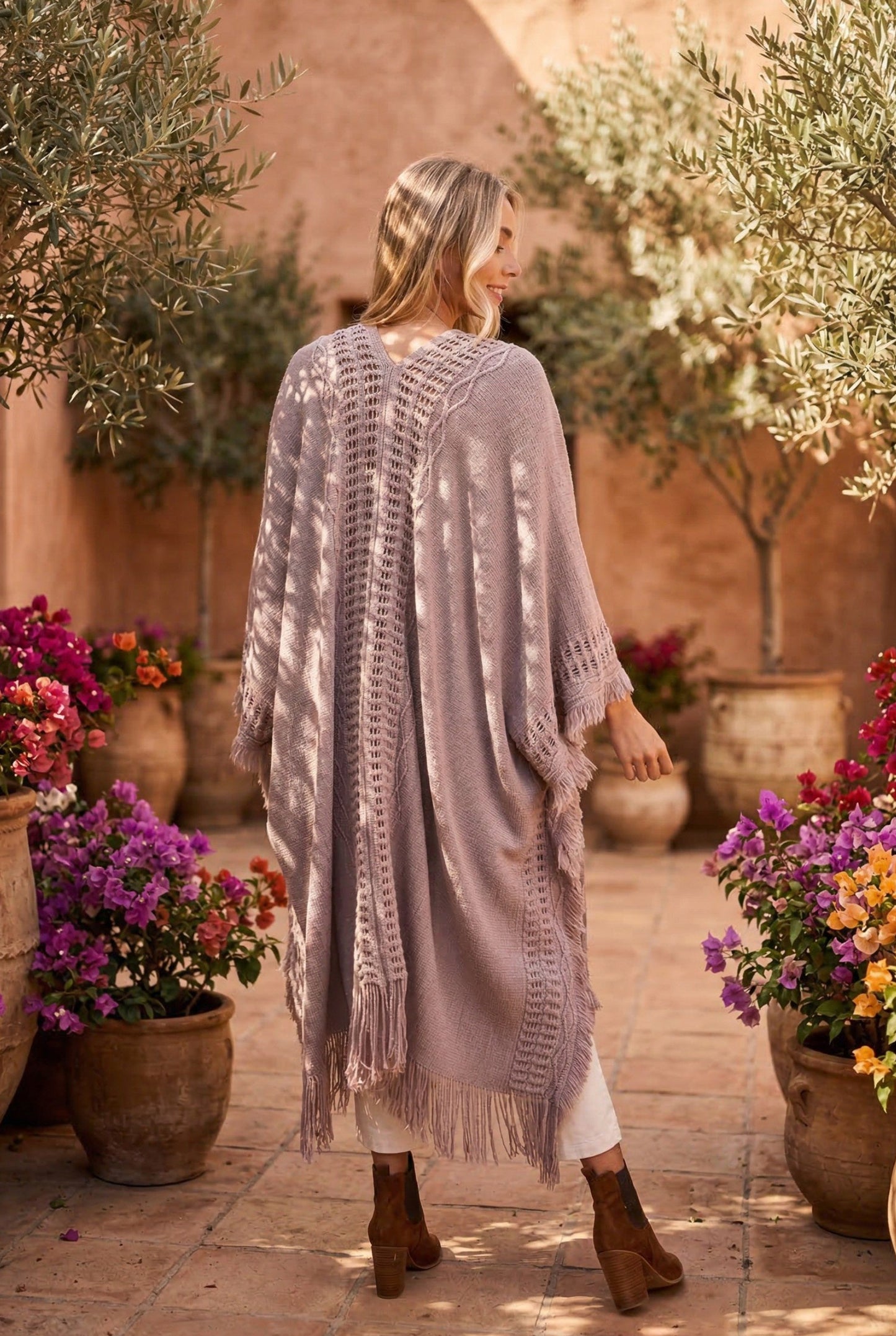 Woman wearing a long, light gray cardigan in a garden setting with flowers and potted plants.