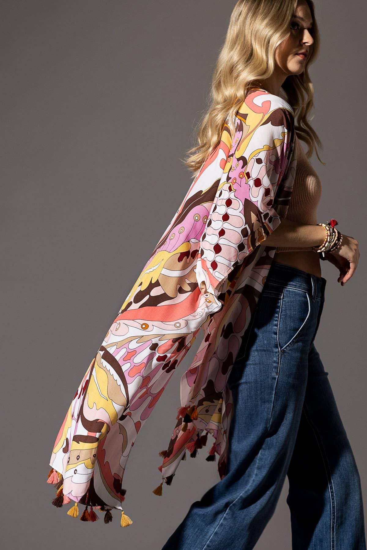 Woman wearing a colorful patterned kimono with tassels against a gray background