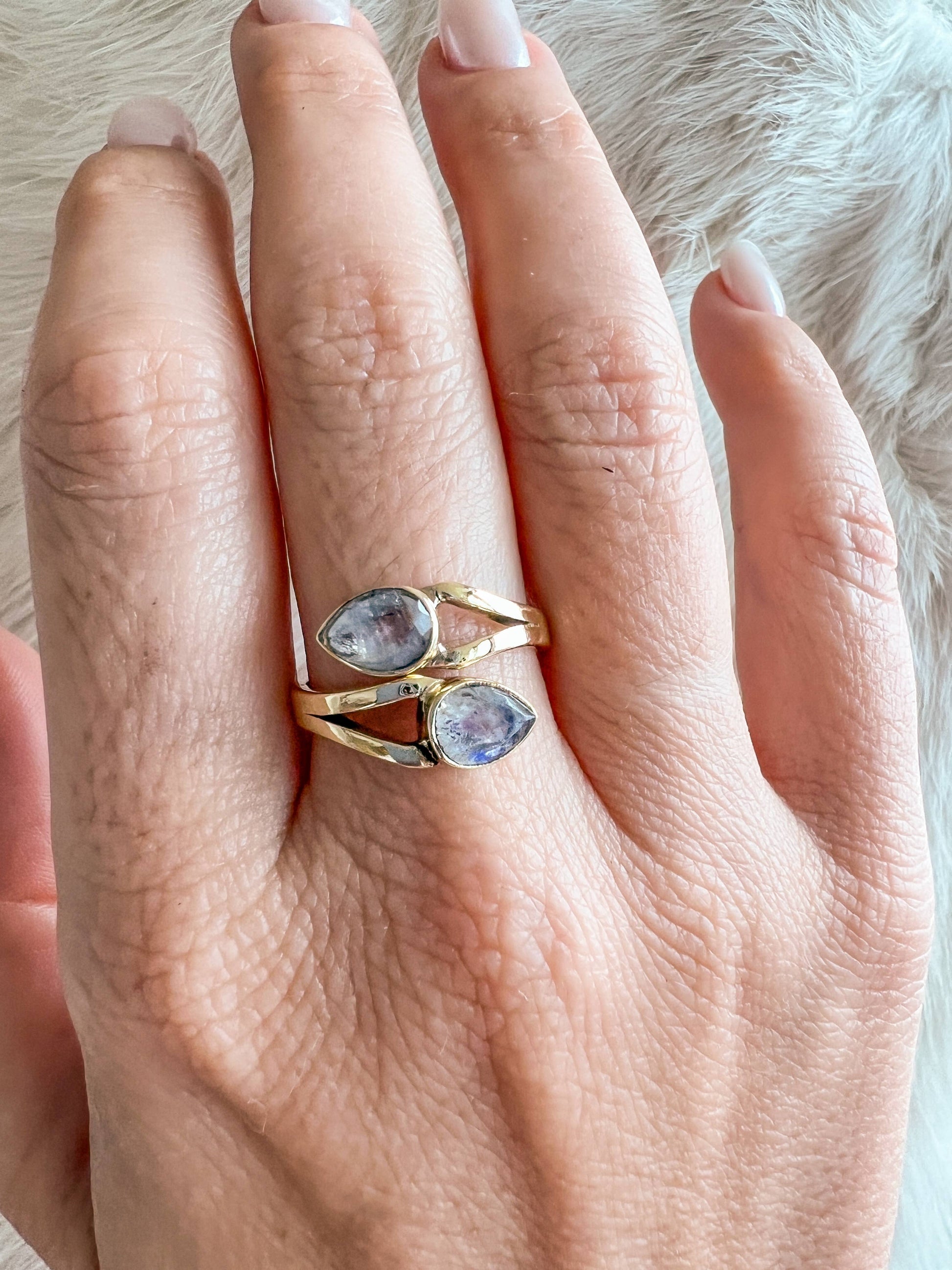 Hand wearing two gold rings with gemstones on a soft fur background