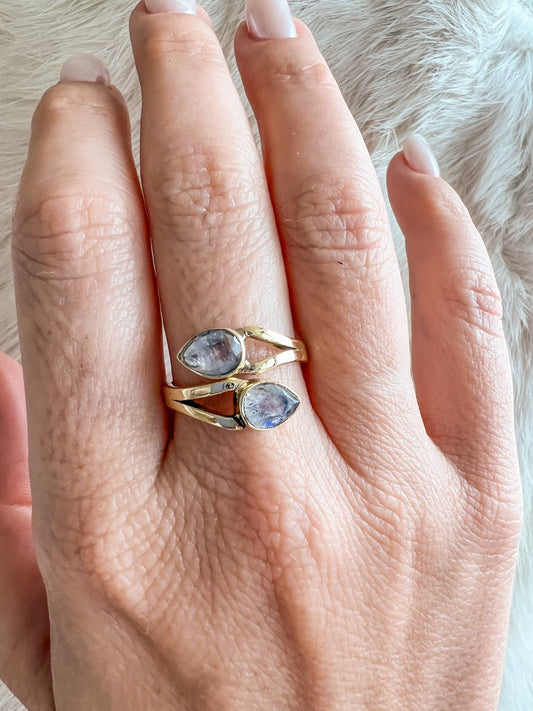 Hand wearing two gold rings with gemstones on a soft fur background