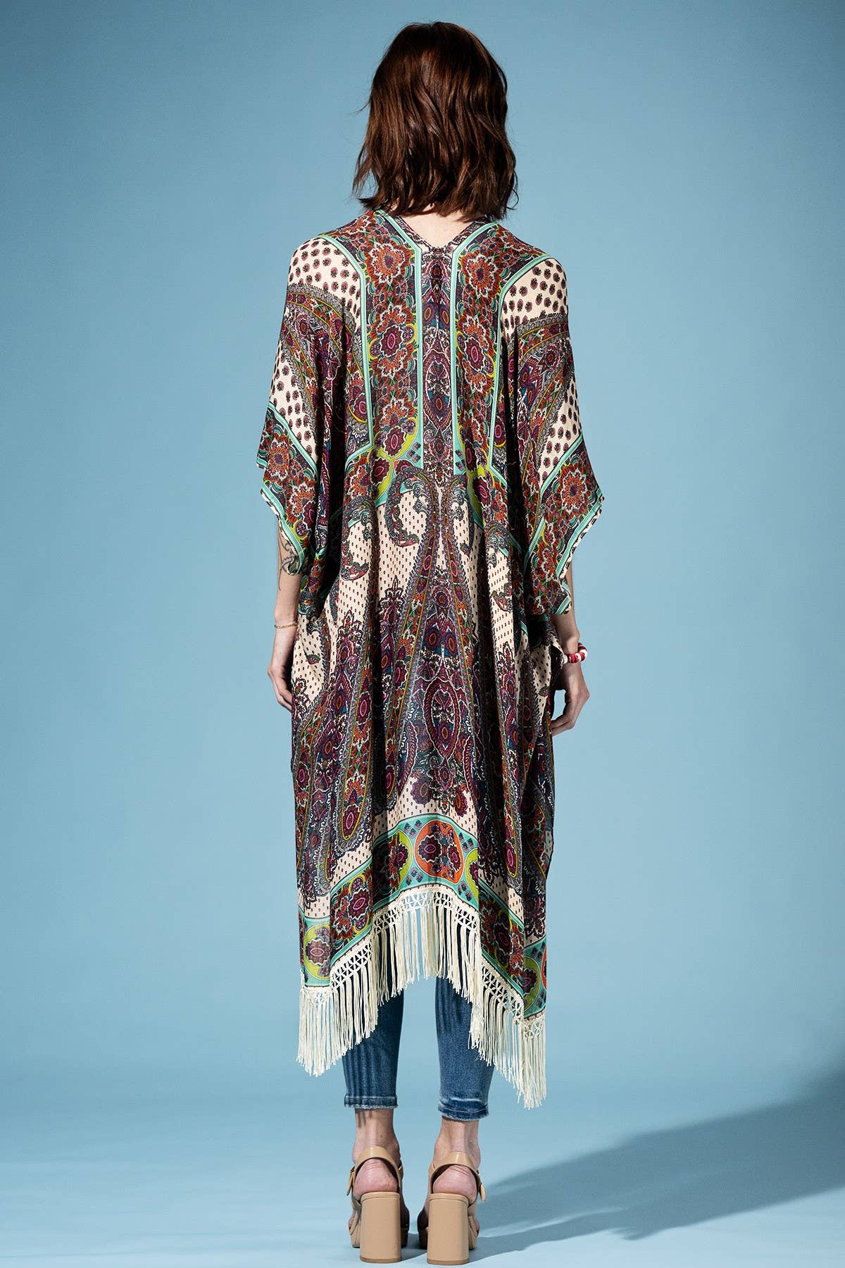 Woman wearing a patterned kimono-style garment with fringe on a blue background