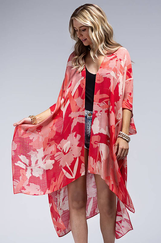 Woman wearing a red floral kimono over a black top and denim shorts on a gray background