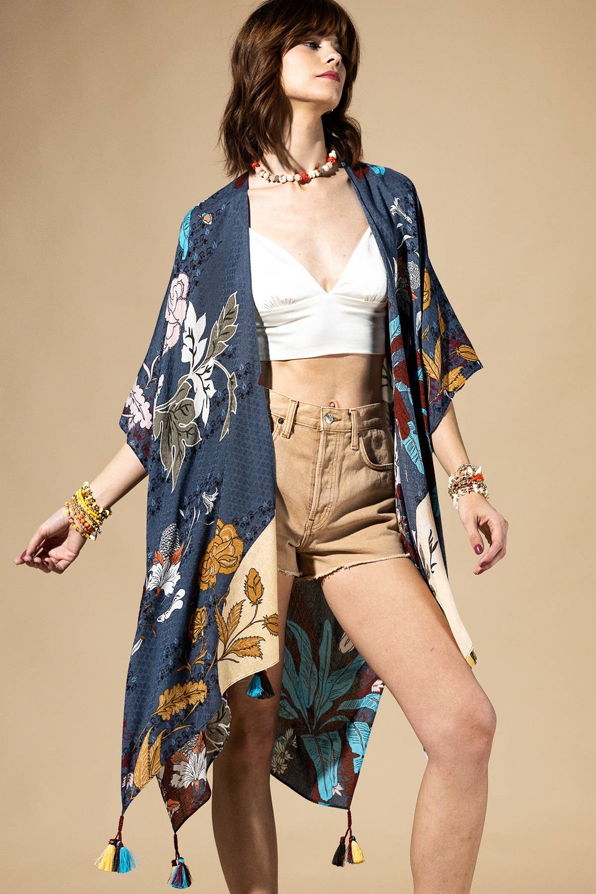Woman wearing a floral kimono over a white top and beige shorts on a beige background