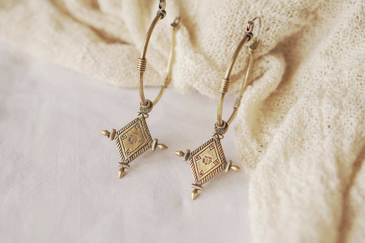 Pair of gold earrings with geometric designs on a textured beige surface