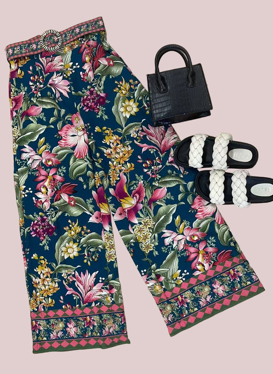 Floral pants with a black handbag and sandals on a wooden floor