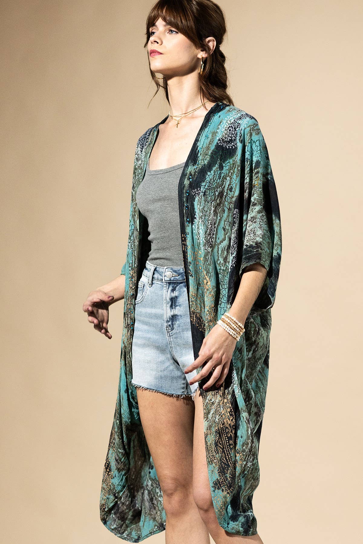 Woman wearing a long, patterned kimono over a casual outfit on a beige background