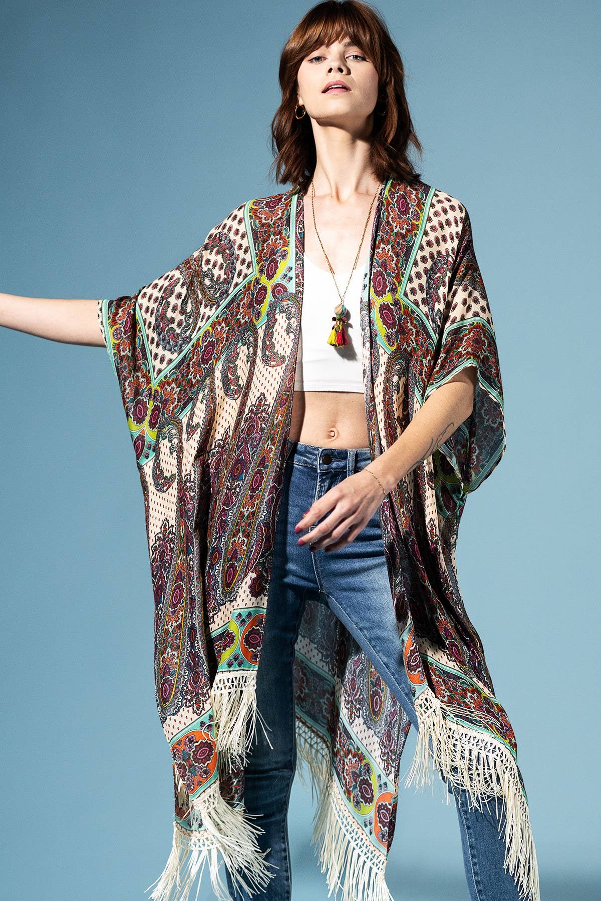 Woman wearing a patterned shawl over a white top and blue jeans on a blue background