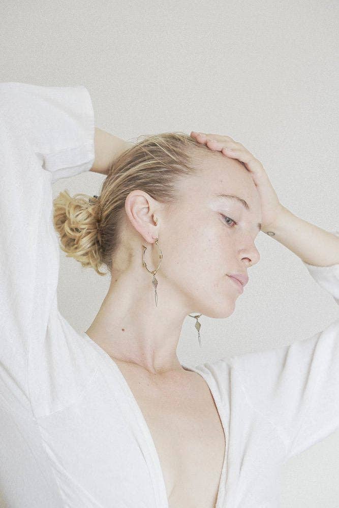 Woman with blonde hair in a bun wearing gold earrings, sitting on a white couch.