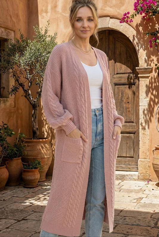 Woman wearing a pink knit cardigan in an outdoor setting with plants and a wooden door.