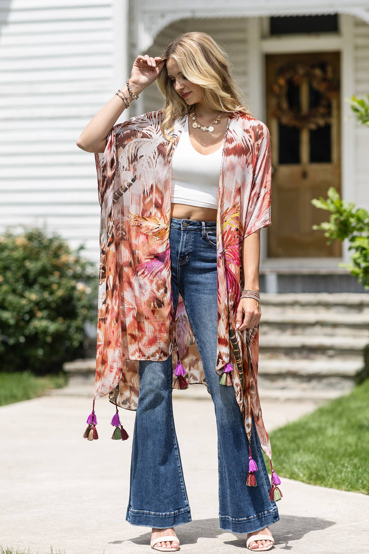 Woman wearing a colorful kimono-style jacket with tassels in front of a house.