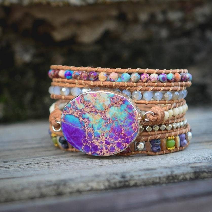 Multicolored beaded bracelet with a large purple stone on a wooden surface, blurred natural background