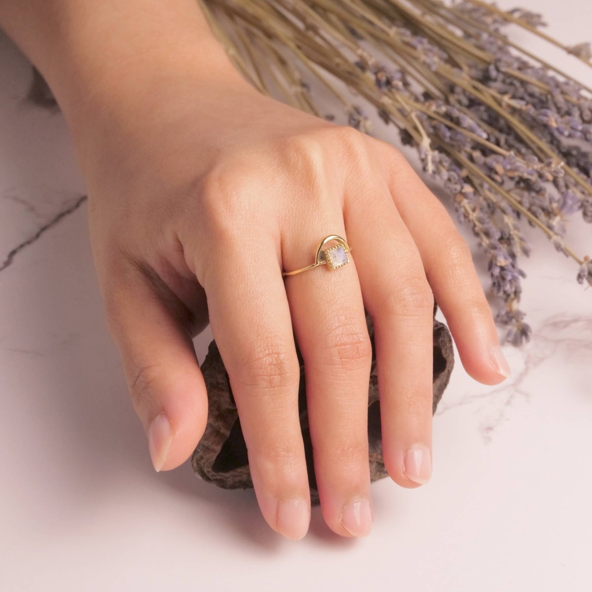 Hand wearing a gold ring with a heart-shaped stone, holding dried lavender flowers.
