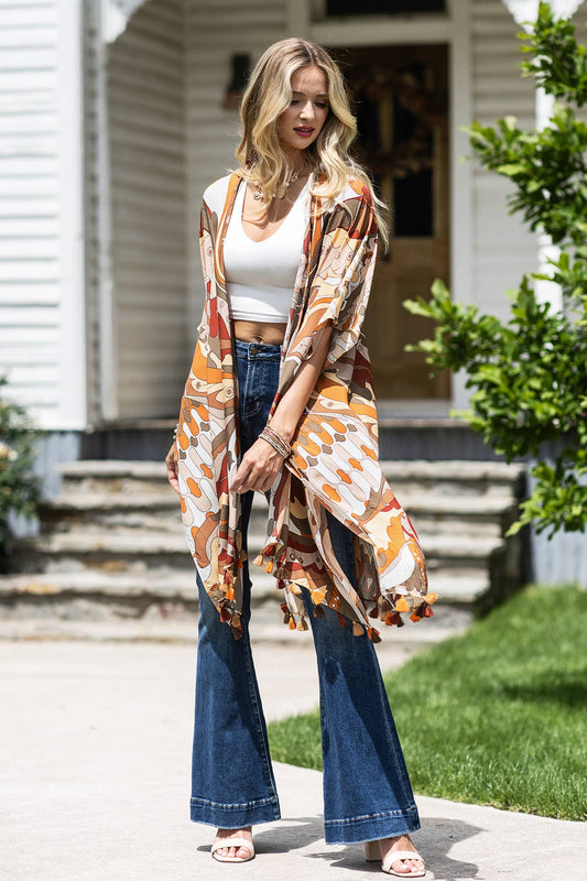 Woman wearing a patterned kimono over a white top and blue jeans, standing outdoors.