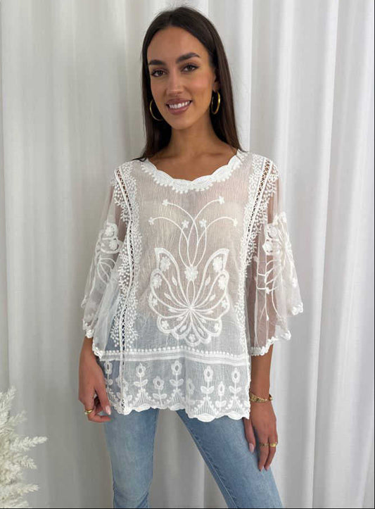 Woman wearing a white lace top and jeans against a white curtain background