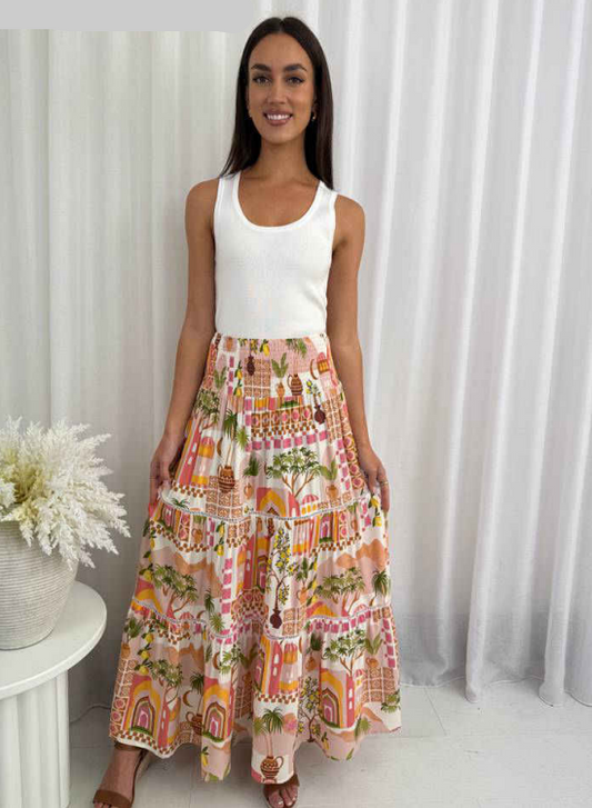 Woman wearing a white top and colorful skirt with a white curtain background