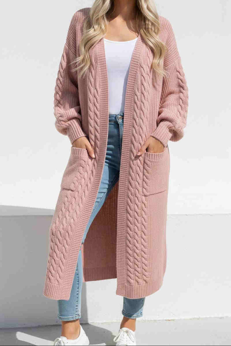 Person wearing a long pink knit cardigan over a white top and blue jeans on a white background.