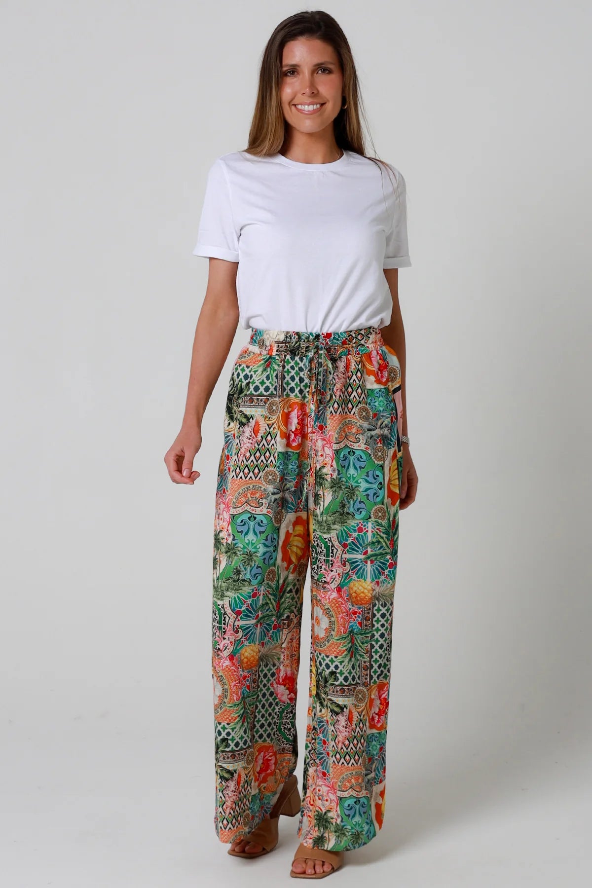 Woman wearing colorful patterned pants and a white shirt on a plain background