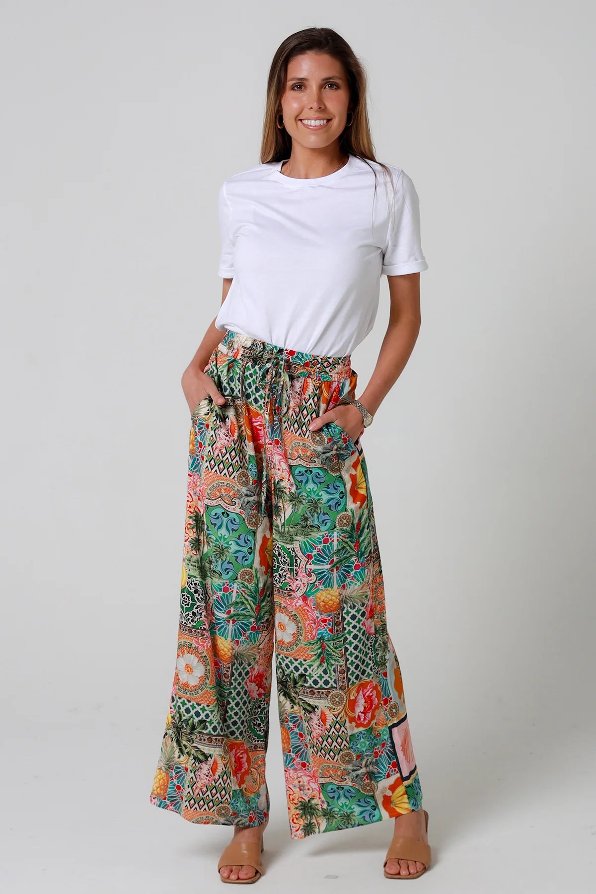 Woman wearing colorful patterned pants and a white shirt on a plain background