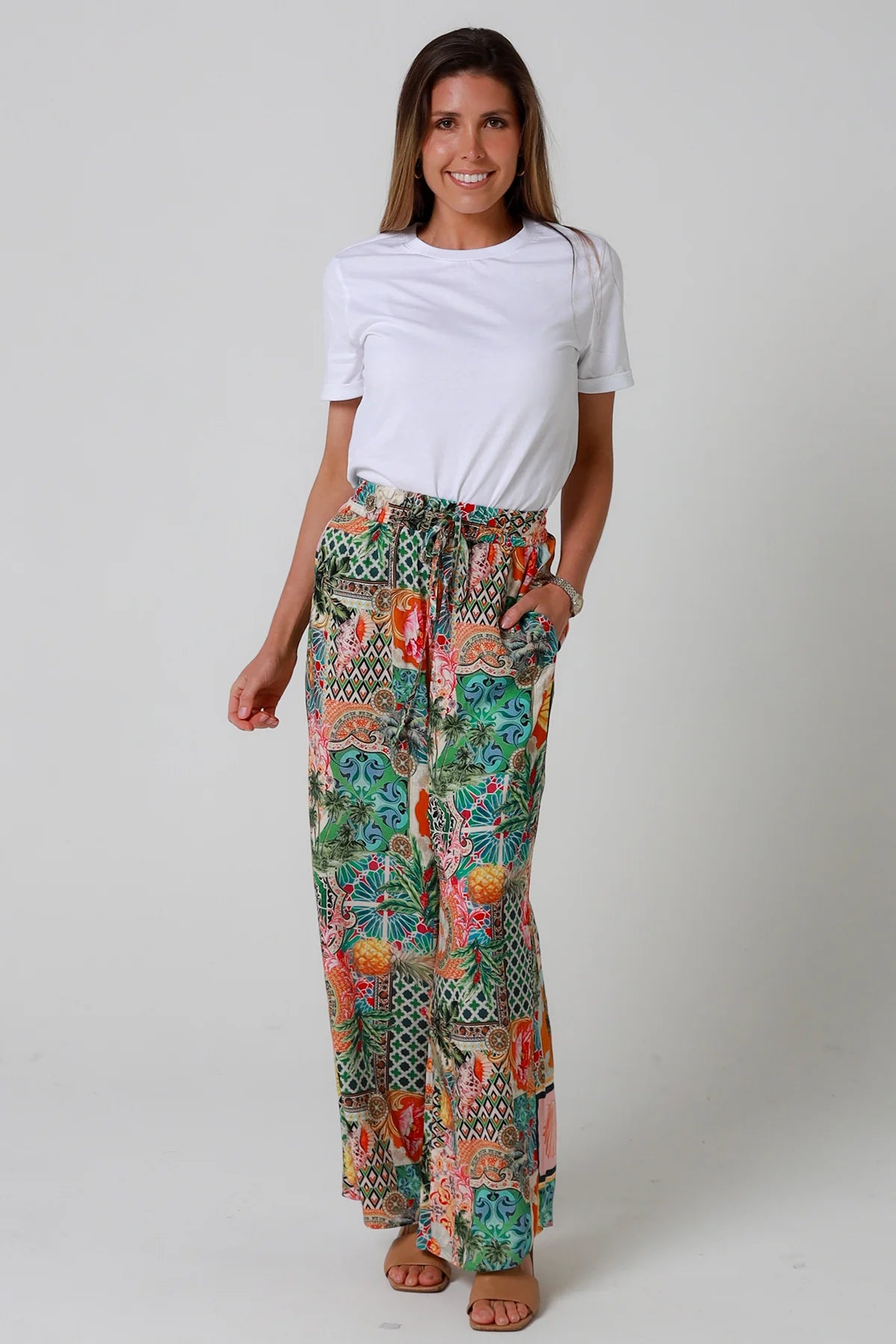 Woman wearing a white t-shirt and colorful patterned pants on a plain background