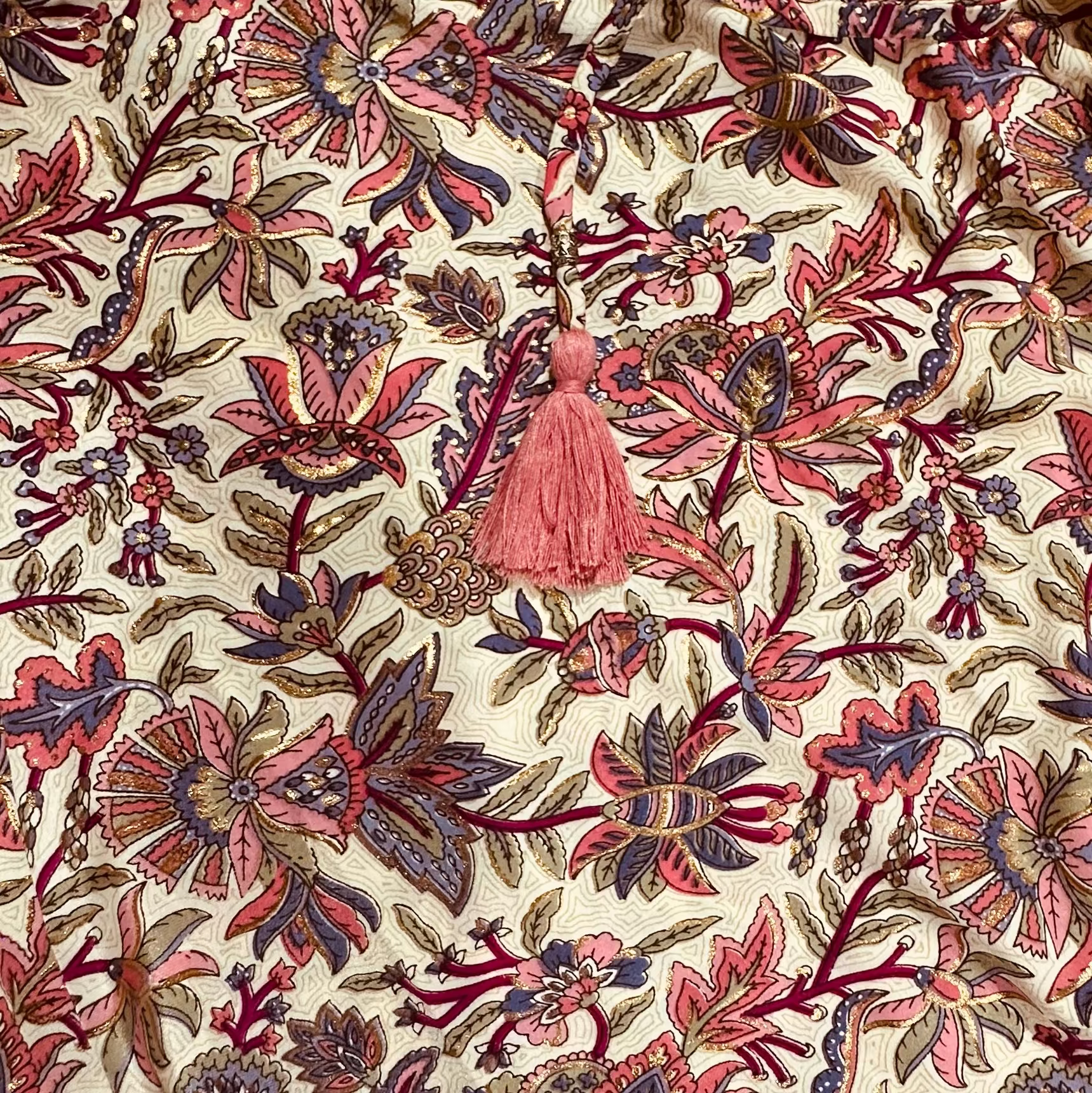 Decorative fabric with floral and leaf patterns in red, pink, and brown on a beige background.