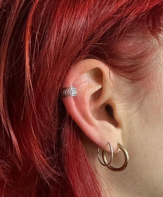 Close-up of an ear with a silver ring and gold hoop earrings, red hair partially visible