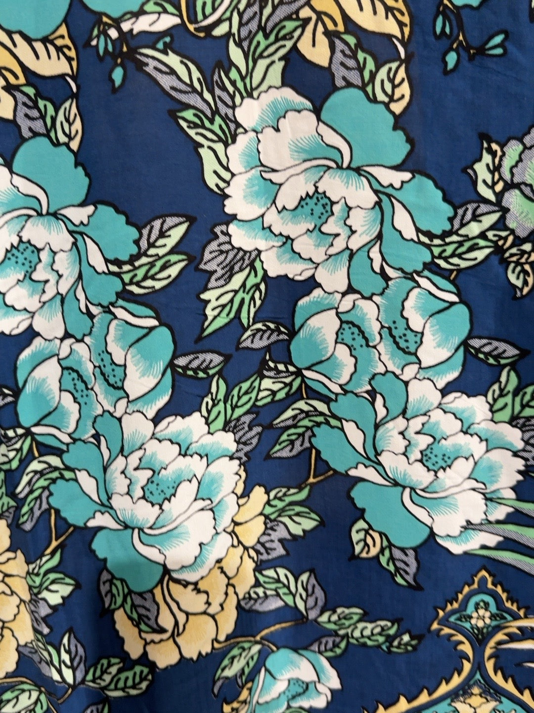 A close-up of a navy blue fabric featuring a large-scale floral print with white and turquoise peonies, green leaves, and touches of yellow.