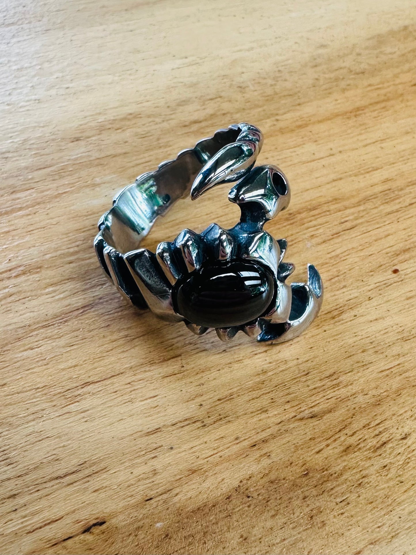 Silver scorpion-shaped ring with a black stone on a wooden surface