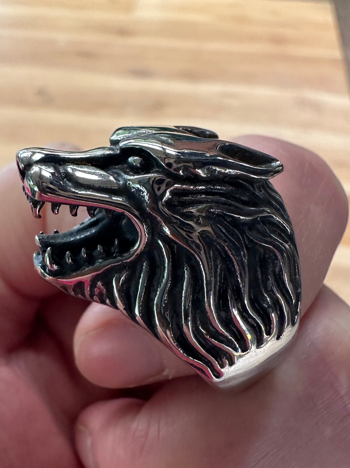 Silver wolf head ring held in a hand with a wooden background