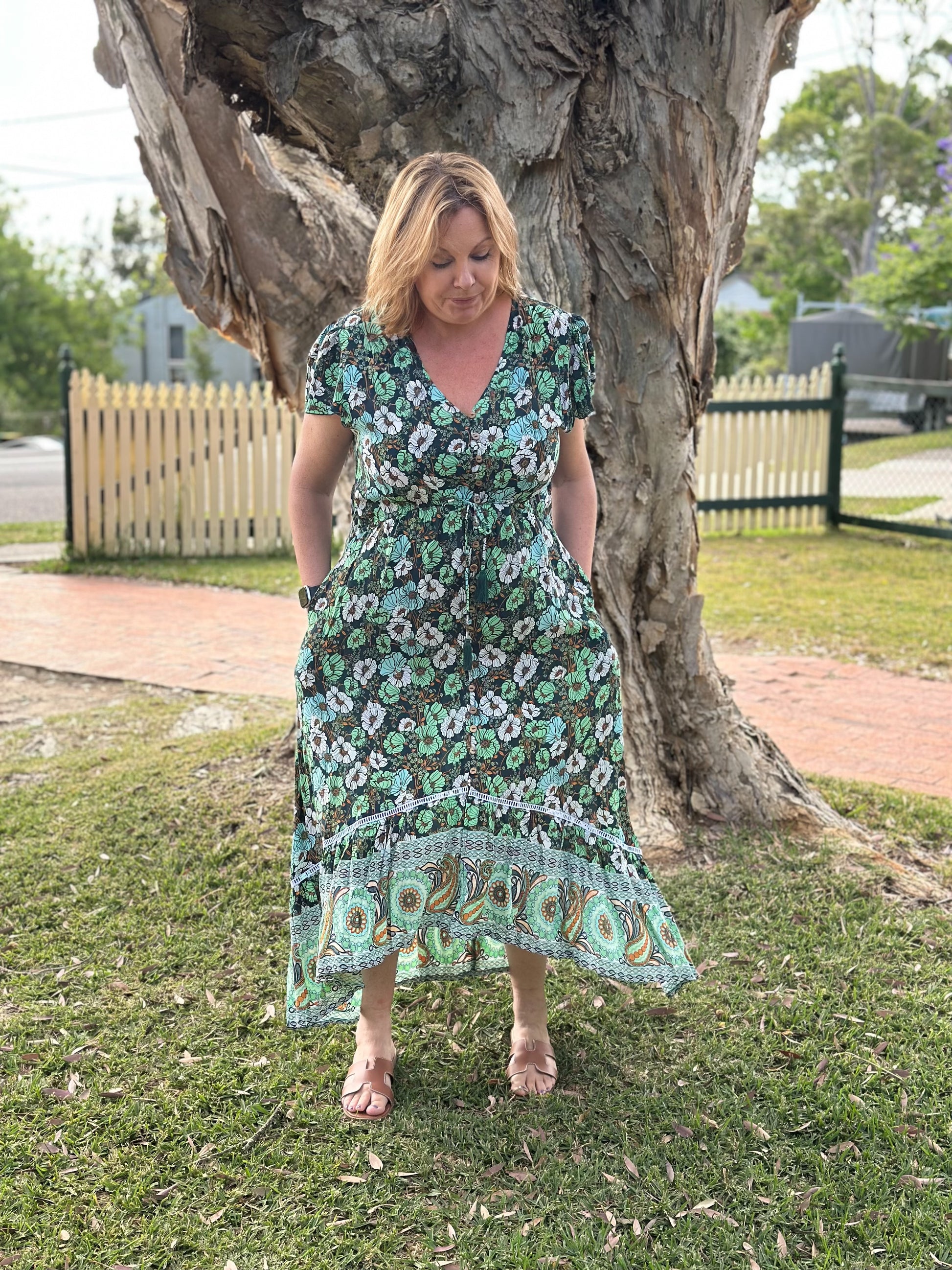 Woman in a floral dress standing under a large tree in an outdoor setting