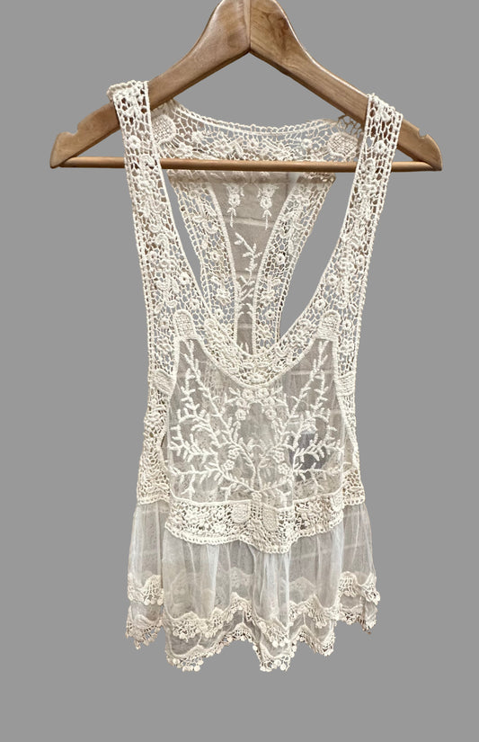 White lace tank top on a wooden hanger against a brick wall.