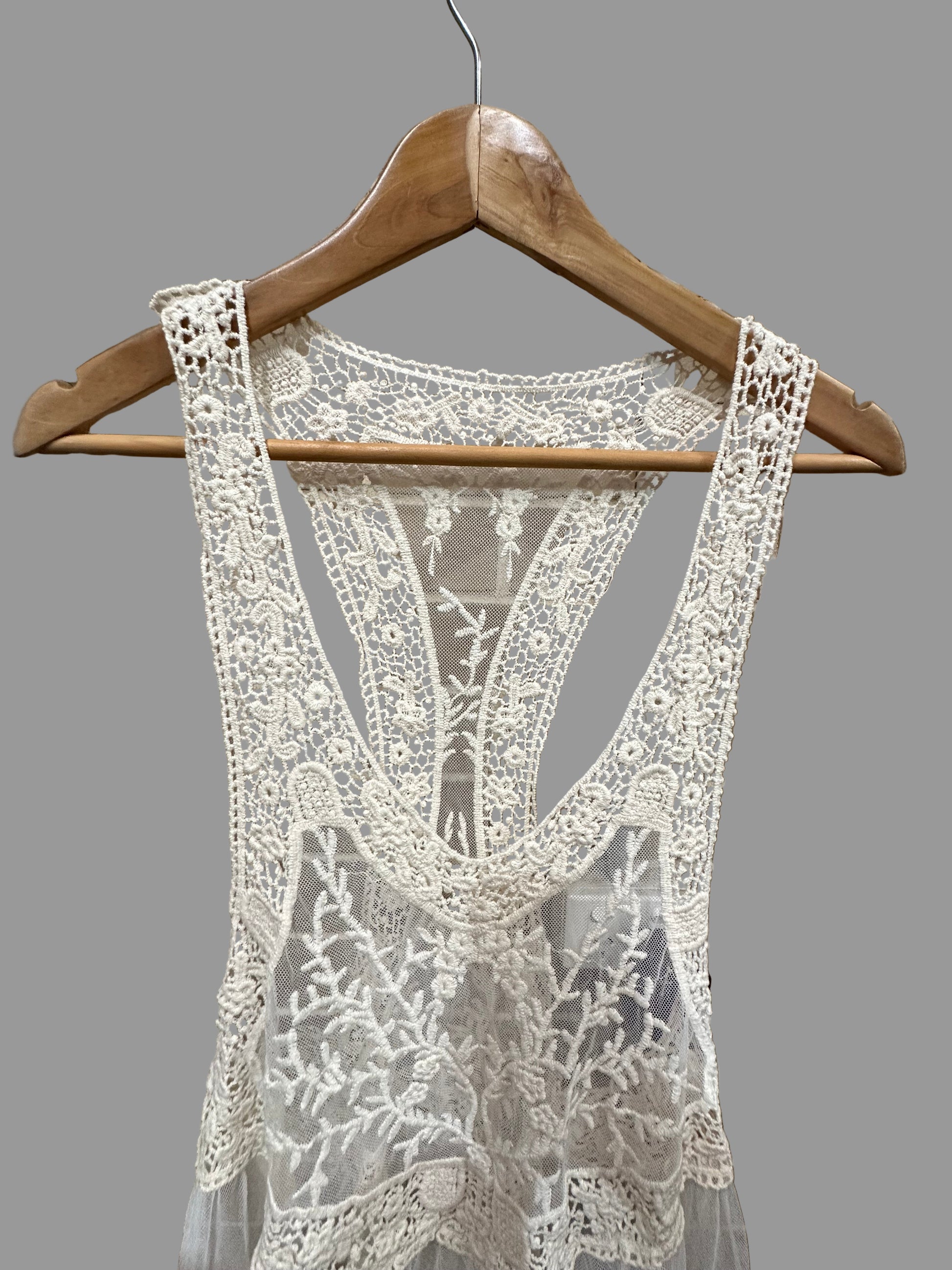 Lace garment on a wooden hanger against a tiled wall.