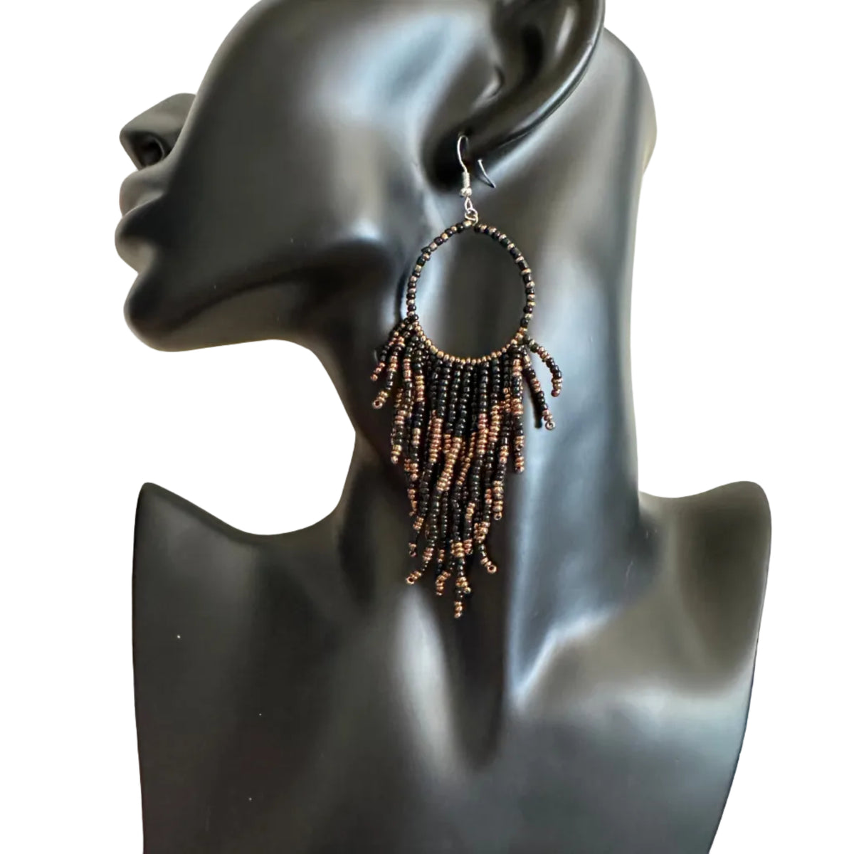 A pair of large hoop earrings with dangling beaded fringe in dark brown and black, displayed on a black mannequin head against a beige wall.