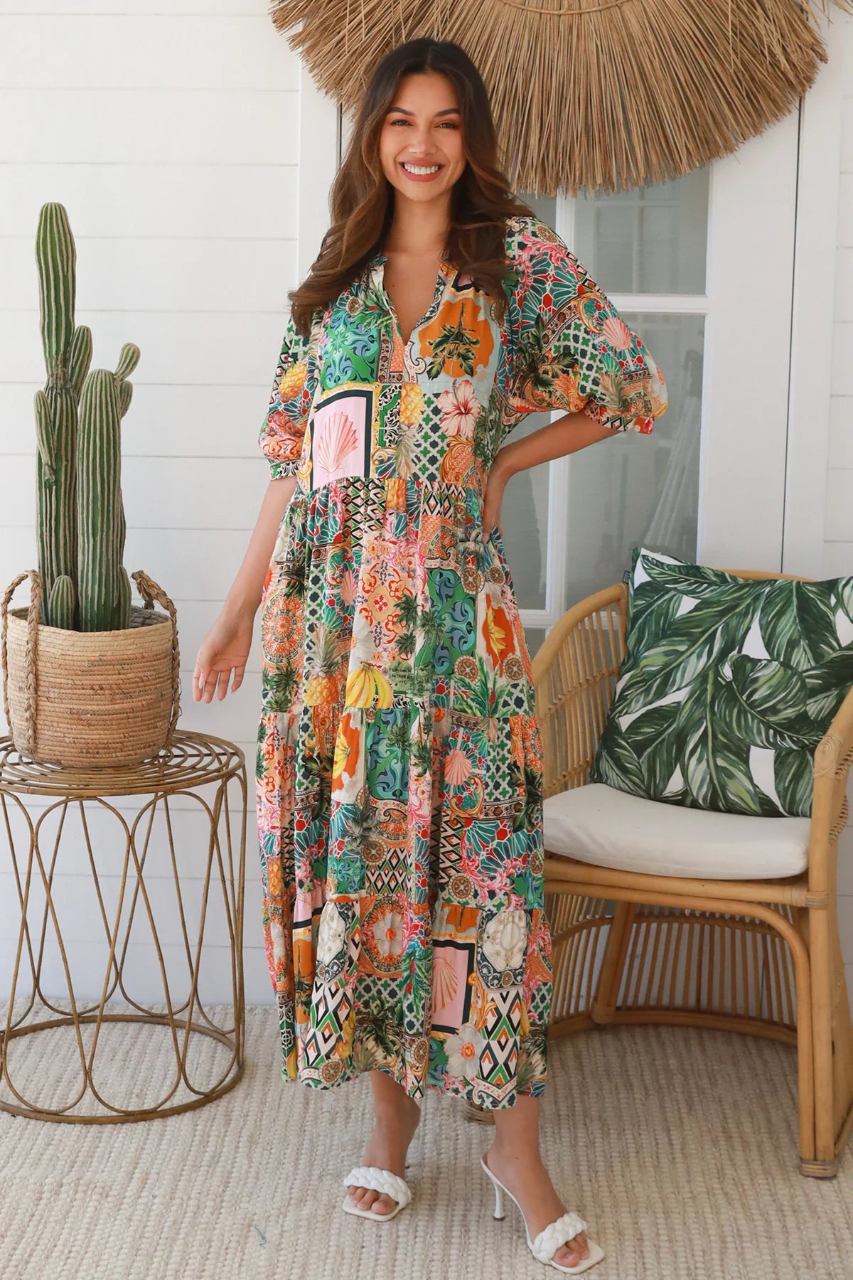 Woman in a colorful dress standing in a room with a cactus plant and wicker chair.