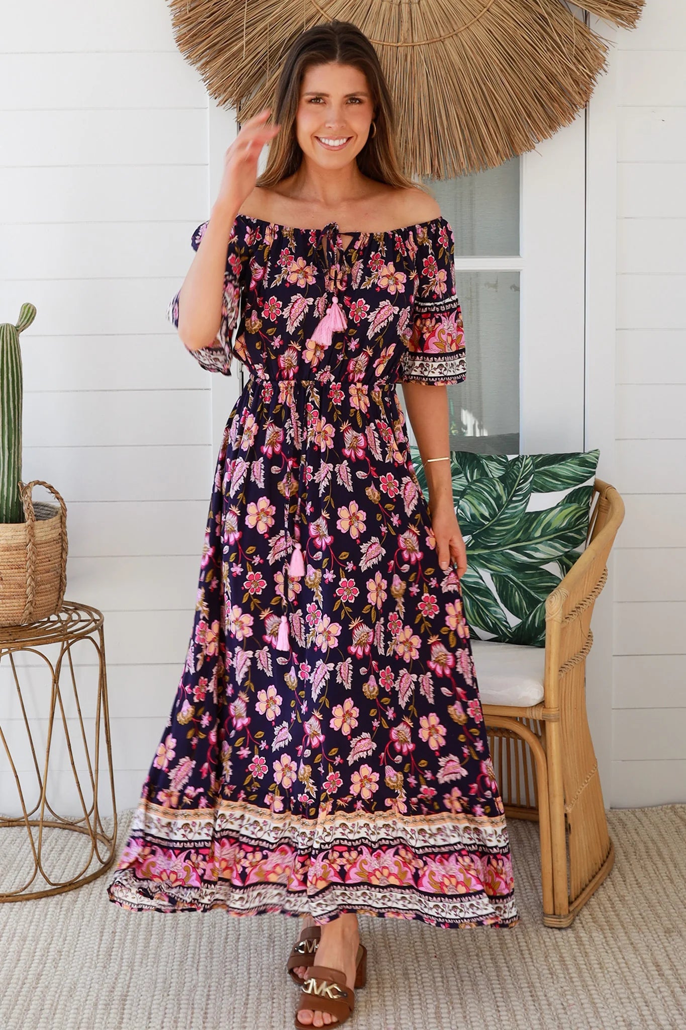 Woman wearing a floral off-shoulder dress holding a straw hat indoors.