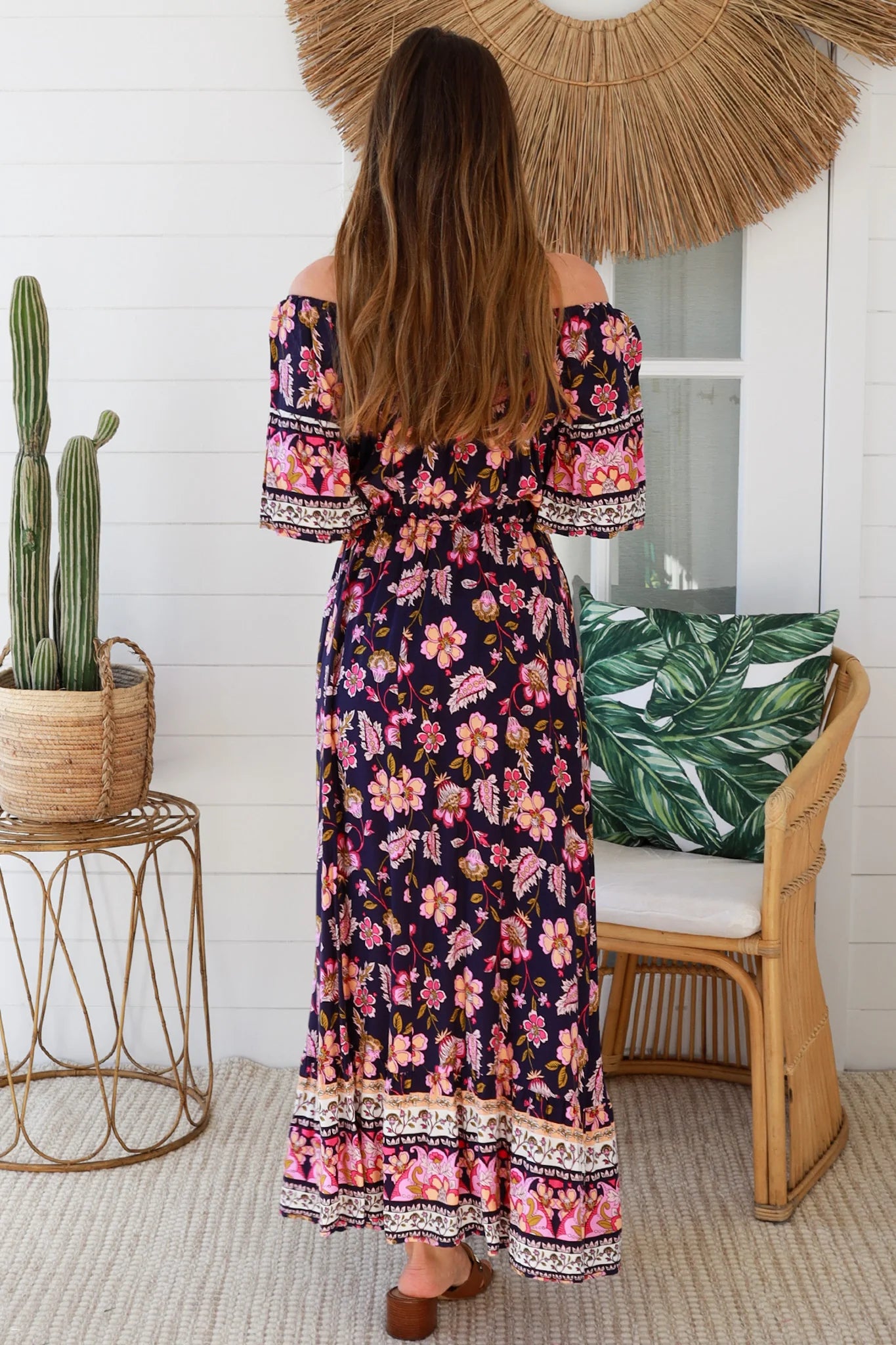 Woman in a floral dress standing in a room with a cactus plant and decorative pillows.