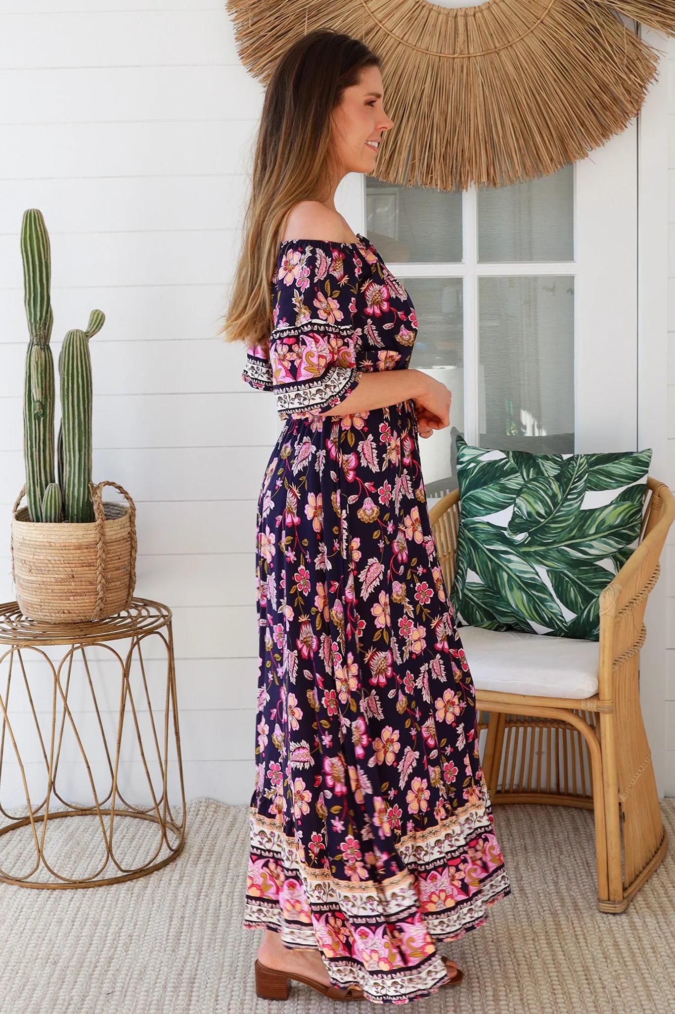 Woman in a floral dress standing in a room with a cactus plant and wicker chair.