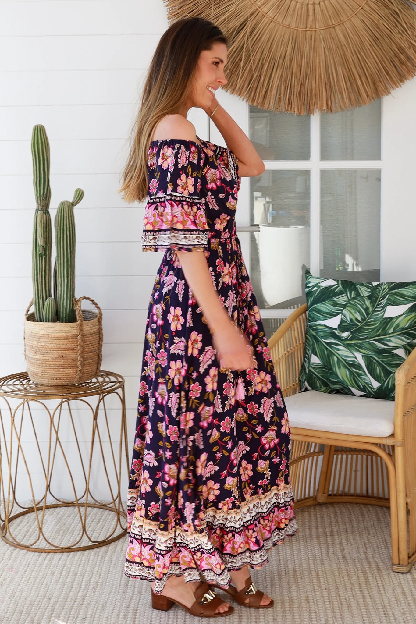 Woman in a floral dress standing in a tropical-themed room with plants and furniture.